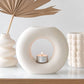 Three ceramic vases with a candle on a white surface