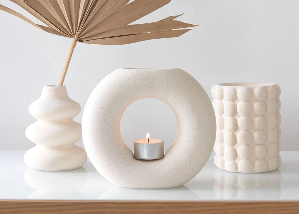 Three ceramic vases with a candle on a white surface